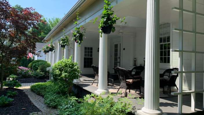 Ein weißes Haus mit einer Veranda und Stühlen darauf