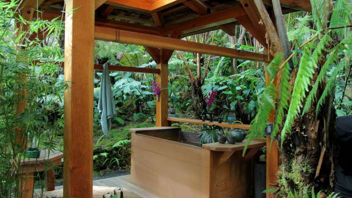 Eine Holzbadewanne unter einem Holzdach im Dschungel