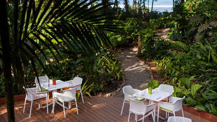 Eine Terrasse mit weißen Tischen und Stühlen inmitten eines tropischen Dschungels