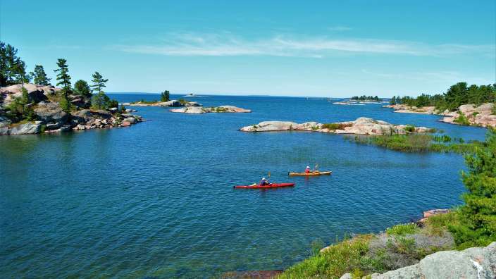 Zwei Menschen paddeln in roten Kajaks auf einem See