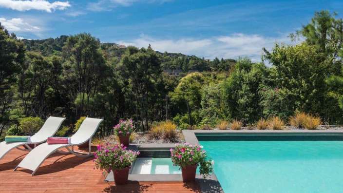 Liegestühle auf einem Holzdeck neben einem Pool mit Bäumen im Hintergrund