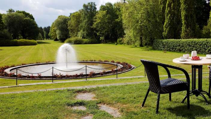 Ein Tisch und ein Stuhl in einem Park mit einem Brunnen im Hintergrund