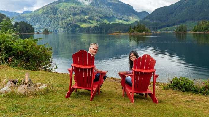Ein Mann und eine Frau sitzen in roten Stühlen am Ufer eines Sees