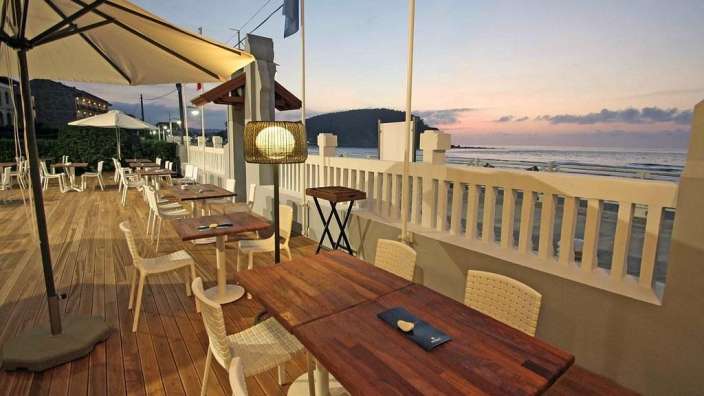 Eine Terrasse mit Holztischen und Stühlen und einem Sonnenuntergang im Hintergrund
