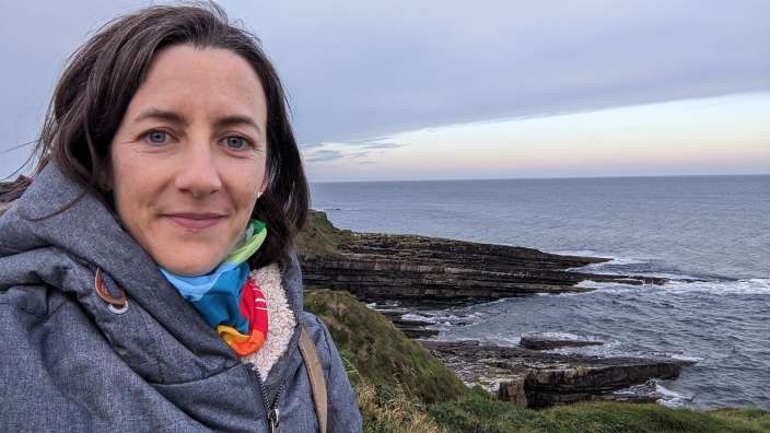 Eine Frau steht auf einer Klippe mit Blick auf das Meer