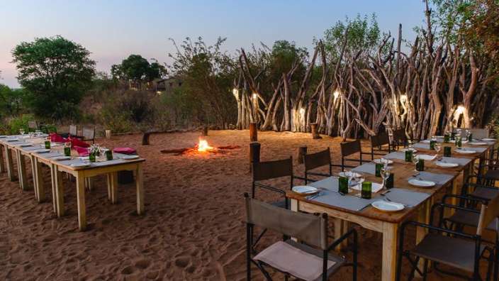 Tische und Stühle im Sand mit einem Feuer im Hintergrund