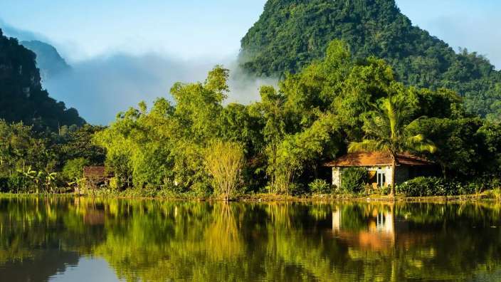 Ein Haus steht am Ufer eines Sees, umgeben von Bäumen und Bergen