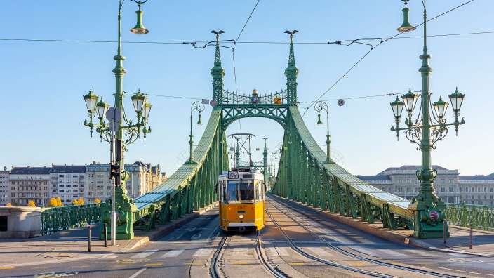 Eine gelbe Straßenbahn fährt über eine grüne Brücke