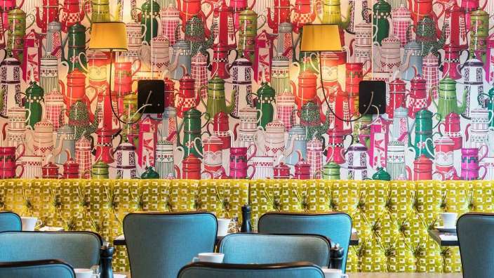 Eine Reihe von Stühlen vor einer bunten Tapete mit Teekannen darauf