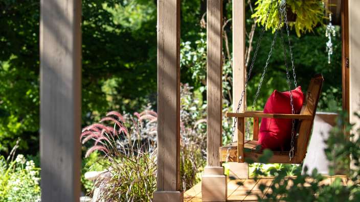 Eine Schaukel auf einer Veranda mit einem roten Kissen darauf