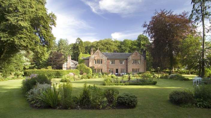 Ein großes Backsteinhaus mit vielen Fenstern umgeben von Bäumen