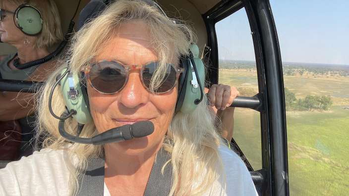 Eine Frau mit Kopfhörern und Sonnenbrille sitzt in einem Hubschrauber