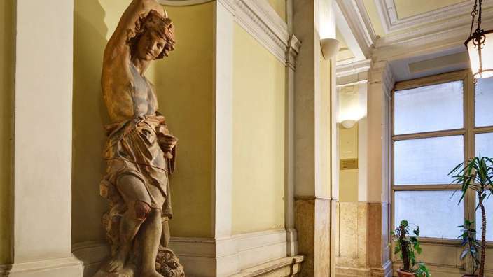 Eine Statue eines Mannes steht an einer gelben Wand