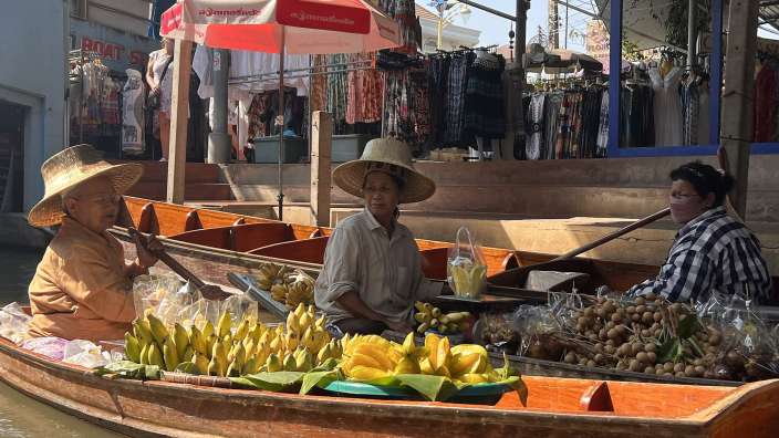 Eine Frau sitzt in einem Boot neben einem Mann und einem roten Regenschirm