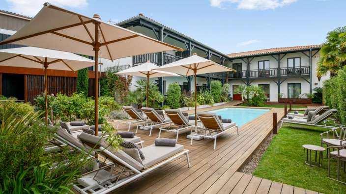 Liegestühle und Sonnenschirme stehen auf einem Holzdeck neben einem Swimmingpool