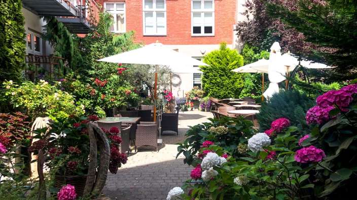 Ein garten mit blumen und tischen und schirmen vor einem roten backsteingebäude