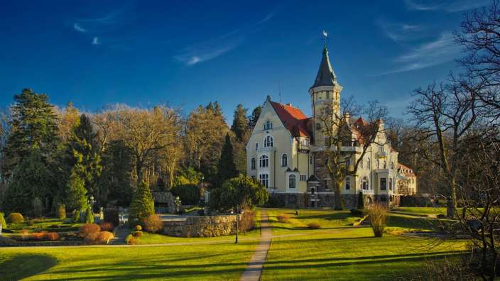 Ein großes weißes Gebäude mit einem roten Dach steht inmitten eines grünen Parks