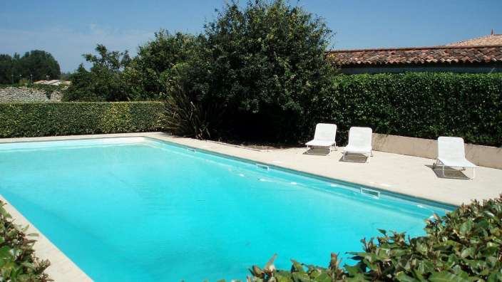 Ein großer Swimmingpool mit drei weißen Stühlen in der Nähe