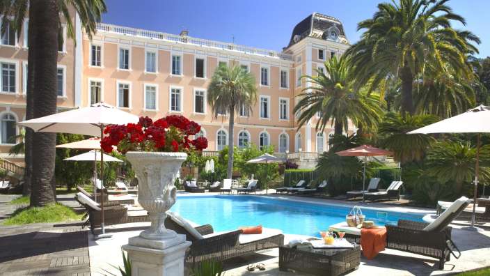 Ein großer Pool mit Liegestühlen und Sonnenschirmen vor einem großen Gebäude