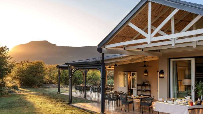 Eine Veranda mit einem Tisch und Stühlen darauf und einem Berg im Hintergrund