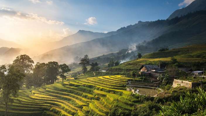 Ein Sonnenaufgang über goldenen Reisterrassen und bergigen Landschaften in Vietnam.