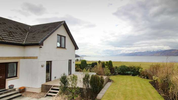 Ein weißes Haus mit einem schwarzen Dach und einem großen Garten mit Blick auf das Meer
