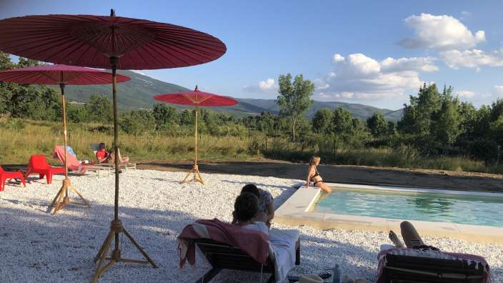 Eine Gruppe von Menschen sitzt neben einem Pool mit Regenschirmen