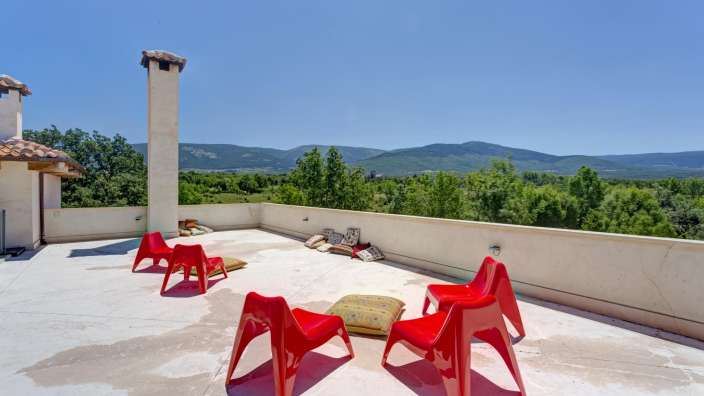 Eine Terrasse mit roten Stühlen und Kissen und Blick auf die Berge