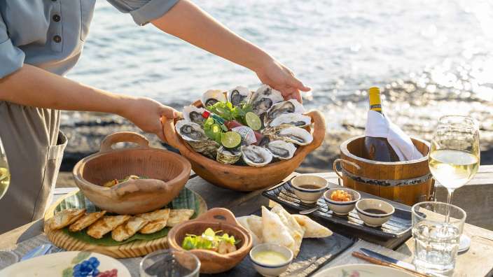 Eine Person hält eine Schale mit Austern und einer Flasche tabasco auf einem Tisch