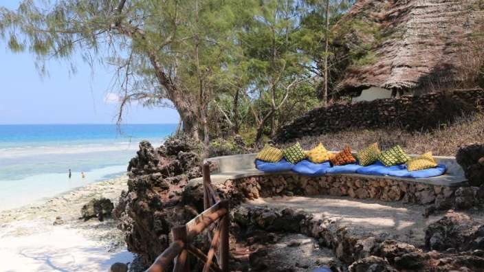 Blaue und gelbe Kissen sitzen auf einer Steinbank am Strand