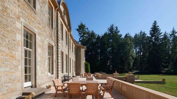 Eine Terrasse mit einem Tisch und Stühlen vor einem großen Steingebäude