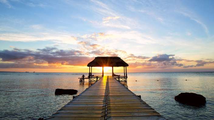 Ein Holzsteg mit einem Strohdach führt ins Meer