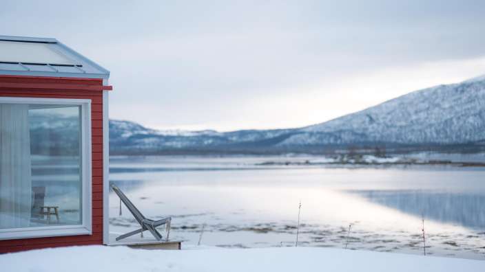 Ein rotes Haus blickt auf einen See mit schneebedeckten Bergen im Hintergrund