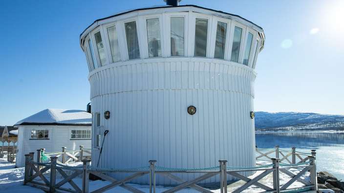 Ein weißer Turm mit vielen Fenstern steht neben einem schneebedeckten See