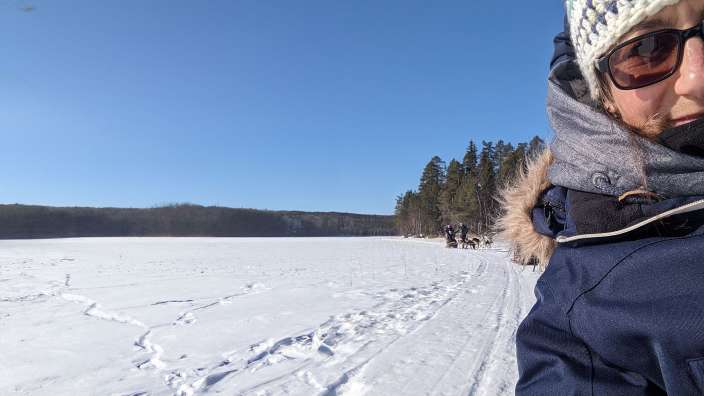 Eine Frau trägt eine Strickmütze und Sonnenbrille, während sie in einem schneebedeckten Feld steht
