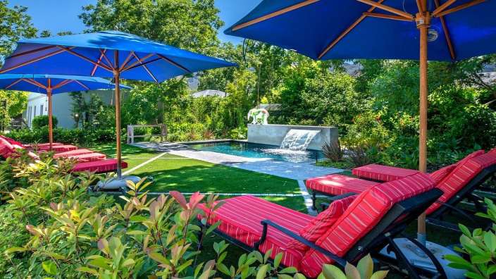 Liegestühle unter blauen Sonnenschirmen neben einem Pool