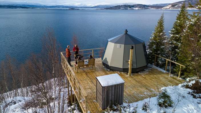Eine Gruppe von Menschen sitzt auf einer Holzterrasse mit Blick auf einen See