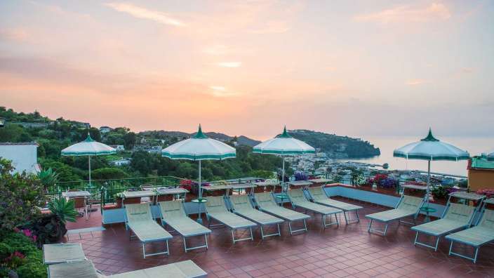 Liegestühle und Sonnenschirme auf einem Dach mit Blick auf den Ozean