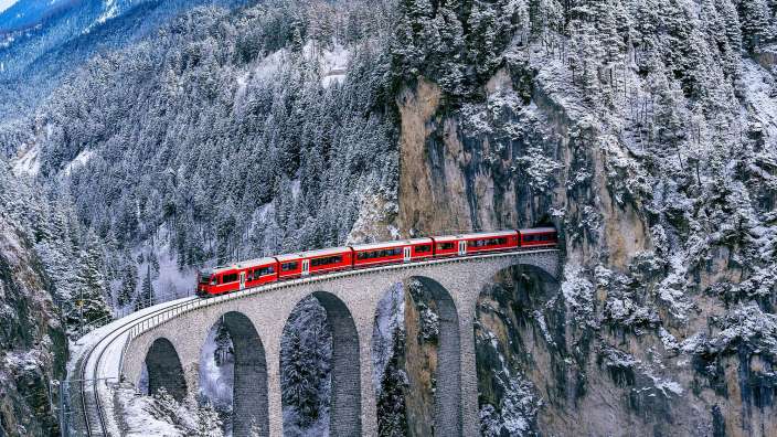 Ein roter Zug fährt über eine Brücke in den Bergen