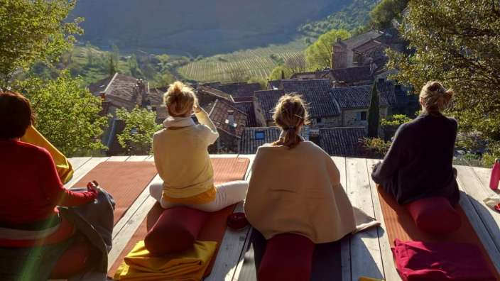 Eine Gruppe von Menschen sitzt auf Yogamatten auf einem Holzdeck