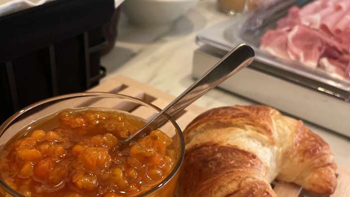 Ein Glas Marmelade neben einem Croissant mit einem Löffel