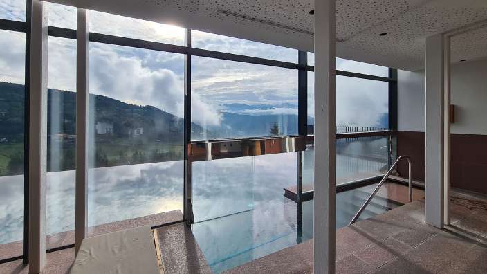 Ein großes Fenster blickt auf einen Pool mit Bergen im Hintergrund