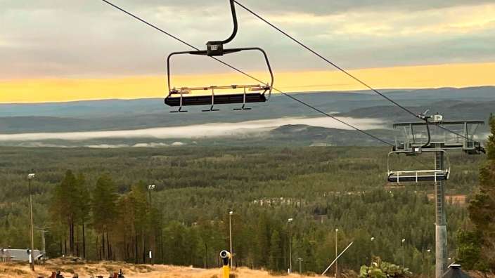 Ein Skilift fährt auf einem Berg mit Bäumen im Hintergrund