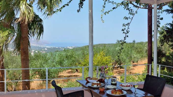 Ein Tisch mit Essen auf einem Balkon mit Blick auf einen Olivenhain
