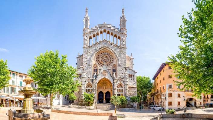 Ein großer Platz mit einem springbrunnen und einer kathedrale mit zwillings türmen und einer großen rosenglasfenster ist auf dem bild.
