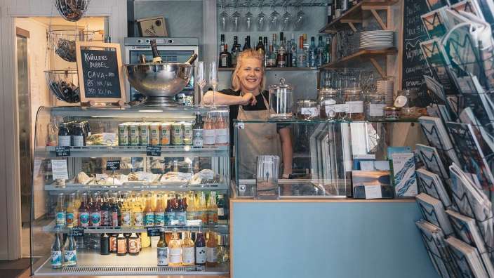 Eine Frau steht hinter einem Schaufenster mit Flaschen und Dosen und einer Auswahl an Getränken
