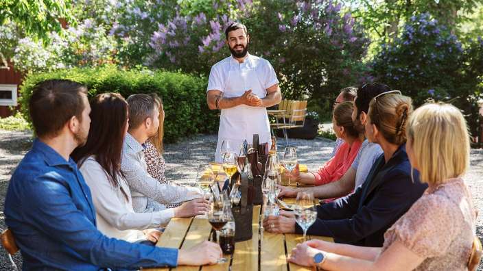 Ein Mann steht vor einer Gruppe von Menschen an einem Tisch