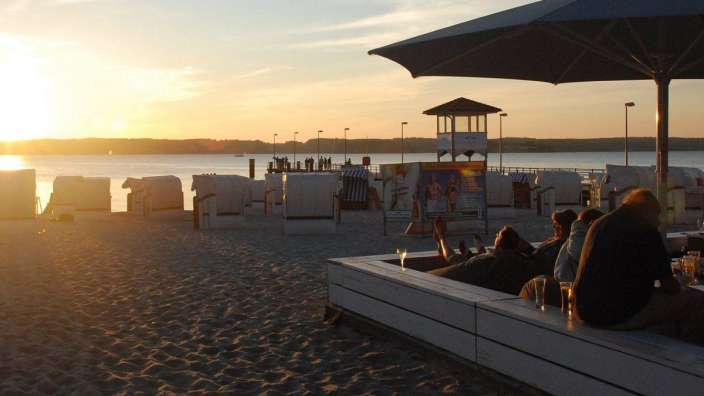 Menschen sitzen auf einer Bank am Strand mit einem Sonnenuntergang im Hintergrund
