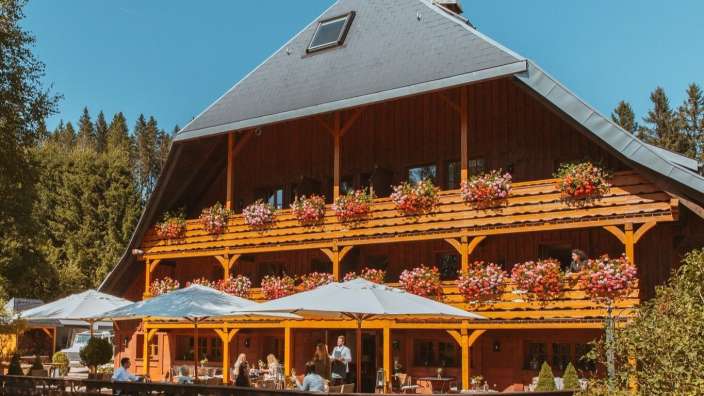 Eine Gruppe von Menschen sitzt auf einer Terrasse vor einem großen Holzhaus