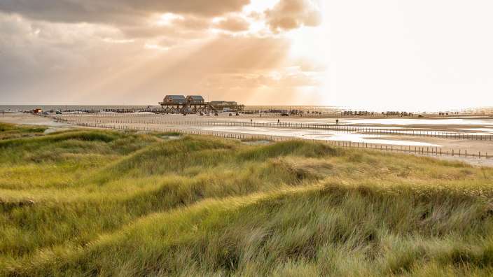 Die Sonne scheint durch die Wolken über einem Strand